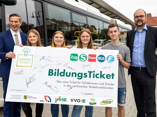 Archivbild von 2021: Martin Dulig und Christian Piwarz halten gemeinsam mit vier Jugendlichen ein großes Schild mit der Aufschrift „BildungsTicket“ vor einem weißen Linienbus. Das Schild trägt die Logos sächsischer Verkehrsverbünde und zahlreiche Unterschriften.