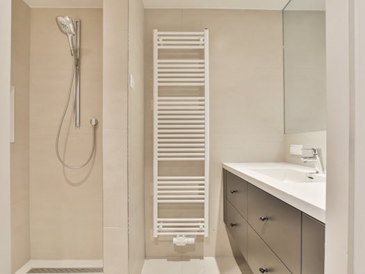 Ein modern gestaltetes, helles und barrierefreies Badezimmer mit ebenerdiger Dusche und Sicherheitsgriffen.