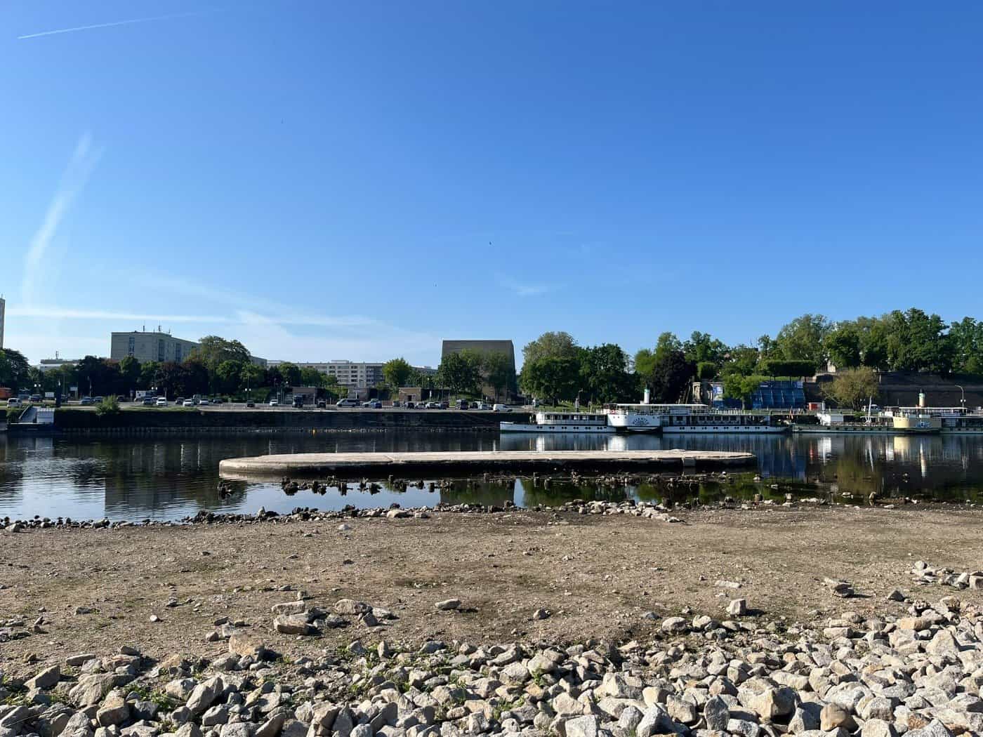 Blick über die Elbe auf den aktuellen Standort der Carolabrücke in Dresden bei blauem Himmel.