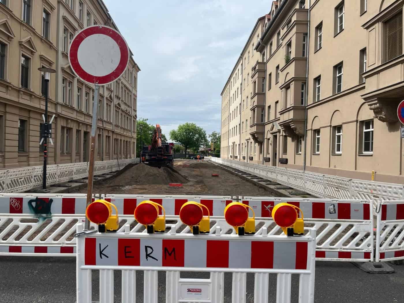 Ein Baustellenschild der Stadt Dresden steht am Straßenrand vor einem Wohngebäude. Im Hintergrund ist die abgesperrte Vorwerkstraße zu sehen, auf der Baufahrzeuge und Absperrbaken den Arbeitsbereich markieren. Ein Hinweisschild gibt Informationen zur Vollsperrung und den Einschränkungen für den Verk