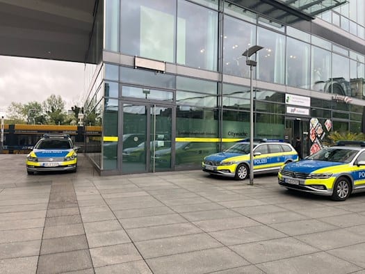 Eingang der Citywache Dresden im Erdgeschoss eines modernen Glasgebäudes (Prager Spitze). Drei blau-silber-gelbe VW Passat Polizeiautos der sächsischen Polizei sind davor geparkt. Schilder an der Tür weisen auf Landeshauptstadt Dresden und Polizeidirektion hin.