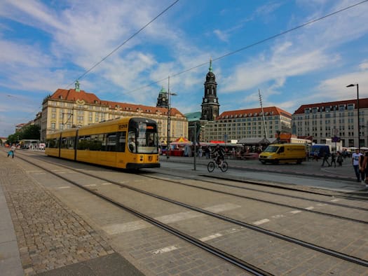 Eine gelbe Straßenbahn der DVB fährt über den Dresdner Altmarkt in Richtung Postplatz, im Hintergrund sind die Kreuzkirche und historische Gebäude unter blauem Himmel zu sehen.