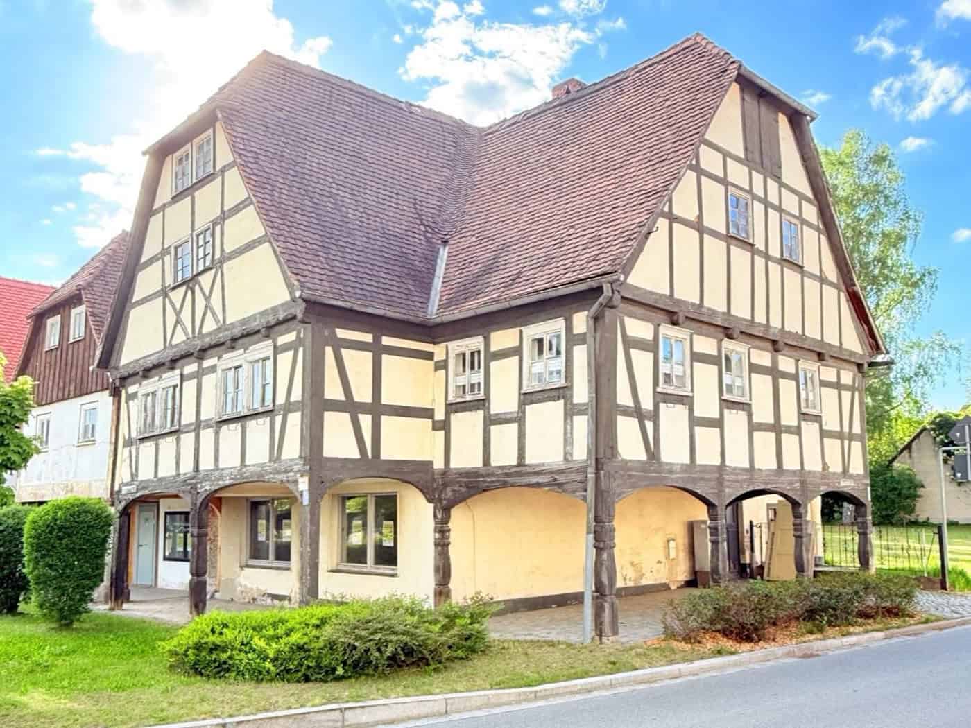 Foto: Ein relativ großes Fachwerkhaus, das schon sehr alt aber renoviert aussieht, steht an einer Straße. Der Himmel ist blau und leicht bewölkt.