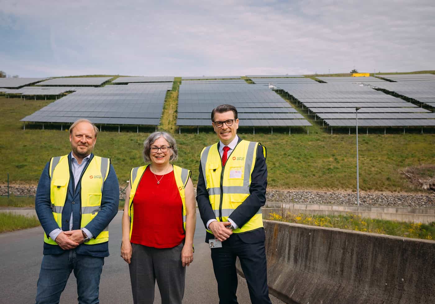 Jens Hirtz, Eva Jähnigen und Dr. Axel Cunow stehen in Sicherheitswesten vor den Solarmodulen des neuen Solarparks an der Radeburger Straße.