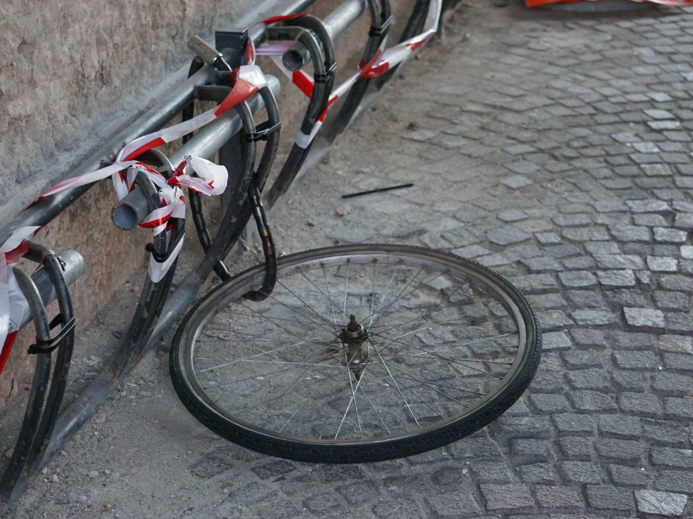 Nahaufnahme eines Fahrradvorderrads, das mit einem massiven schwarzen Kettenschloss an einem metallenen Geländer im urbanen Raum gesichert ist.