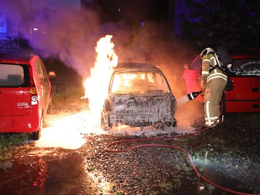 Ein brennender Pkw auf einem Parkplatz während eines Feuerwehreinsatzes, Einsatzkräfte der Feuerwehr Dresden löschen das Fahrzeug unter Atemschutz.