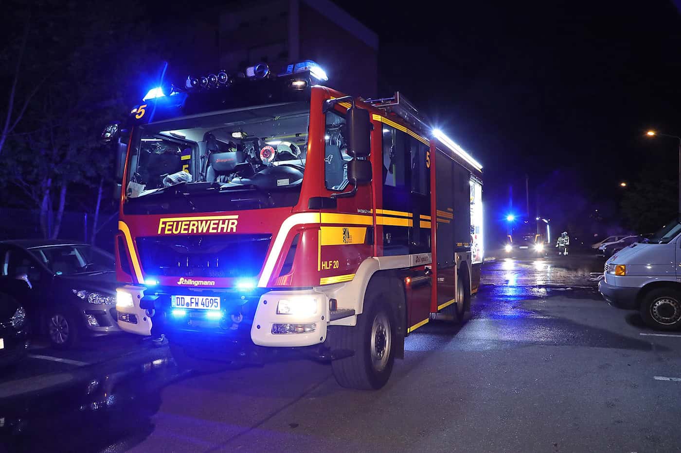 Feuerwehr Dresden: Einsätze in der Mainacht 2026. Nächtliche Aufnahme eines modernen, rot-gelben Feuerwehrfahrzeugs (HLF 20) mit eingeschaltetem Blaulicht. Das Fahrzeug mit dem Kennzeichen DD FW 4095 steht auf einer asphaltierten Straße in der Nähe geparkter Autos; im Hintergrund ist ein weiteres Einsatzfahrzeug mit Blaulicht zu sehen.
