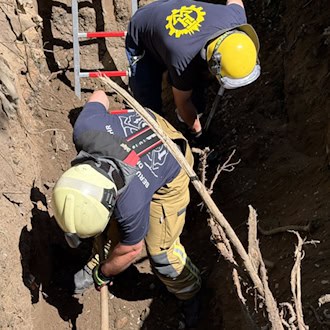 Einsatzkräfte von Feuerwehr und THW graben in einer tiefen Grube, um die im Rohr feststeckende Schäferhündin „Mara“ zu befreien.