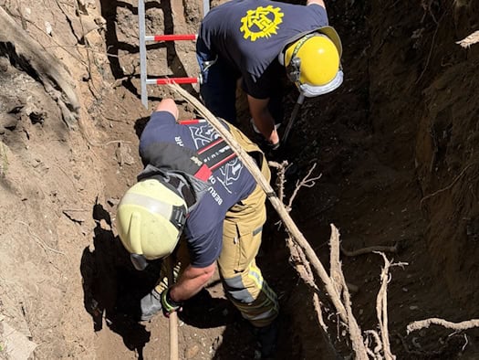 Einsatzkräfte von Feuerwehr und THW graben in einer tiefen Grube, um die im Rohr feststeckende Schäferhündin „Mara“ zu befreien.