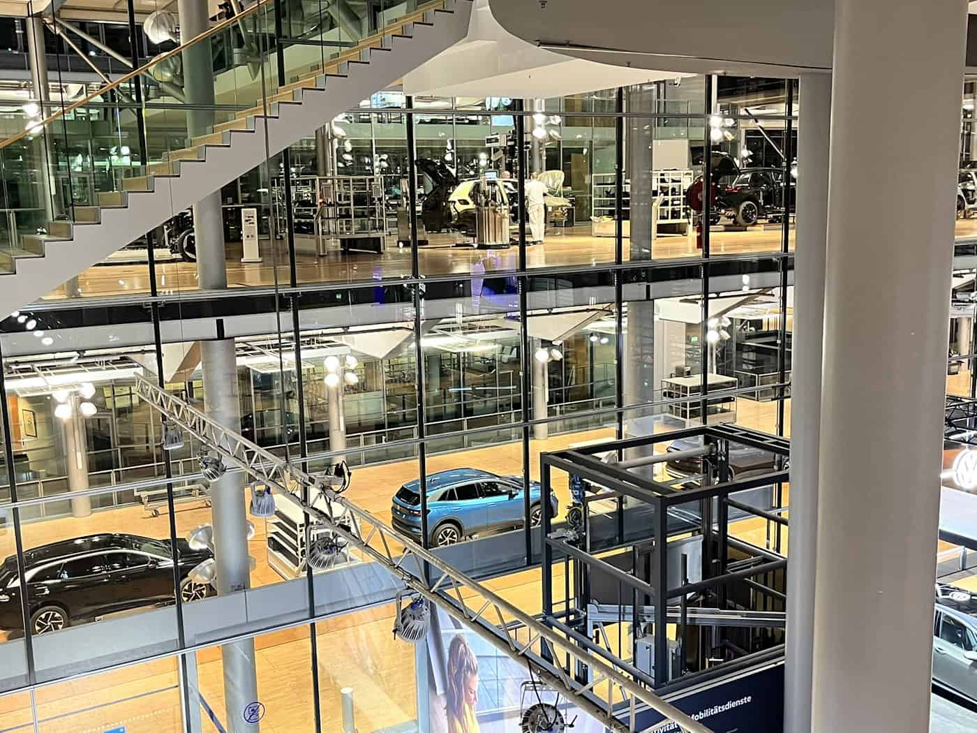 Detaillierte Innenansicht der mehrstöckigen Montagehallen der Gläsernen Manufaktur Dresden. Zu sehen sind die Glasböden, Autos (VW ID Modelle) in verschiedenen Montagestufen, ein komplexes Hebesystem und die Architektur aus Stahl und Glas.