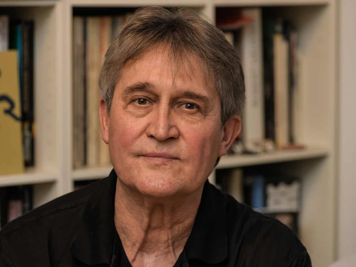 Porträt des Fotografen Matthias Creutziger. Der Künstler blickt ruhig in die Kamera; im Hintergrund ist ein Bücherregal mit zahlreichen Bildbänden und Fachliteratur zu erkennen.
