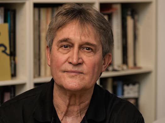 Porträt des Fotografen Matthias Creutziger. Der Künstler blickt ruhig in die Kamera; im Hintergrund ist ein Bücherregal mit zahlreichen Bildbänden und Fachliteratur zu erkennen.