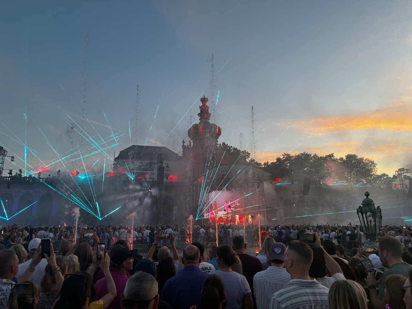 Große Menschenmenge bei einem Open-Air-Konzert von Purple Disco Machine im beleuchteten Innenhof des Dresdner Zwingers mit Lasershow und Wasserfontänen bei Sonnenuntergang.