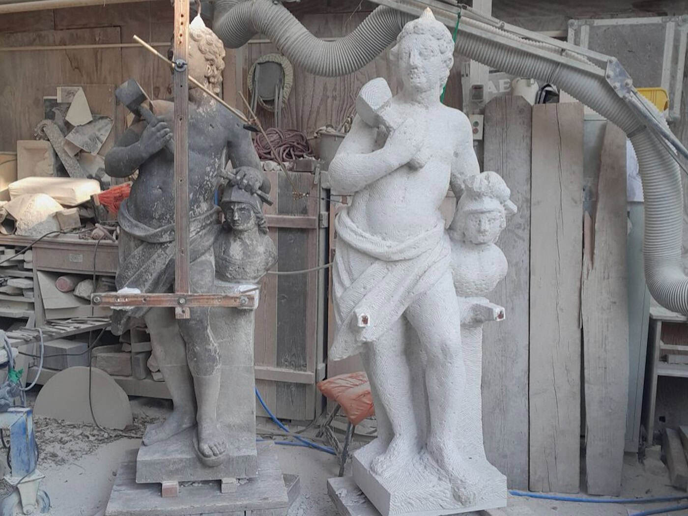 Eine Werkstattaufnahme der barocken Skulptur „Bildhauerei“, links das dunkle Original und rechts die neu angefertigte, helle Sandstein-Kopie, gefertigt im klassischen Punktierverfahren.