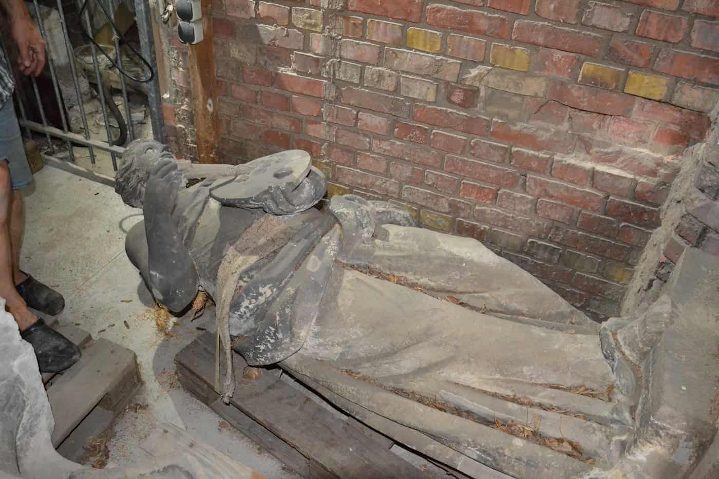 Historisches Original der Skulptur „Malerei“ im Lapidarium Dresden Die historische, dunkle Sandsteinskulptur „Malerei“ liegt geschützt auf einer Holzpalette in der Ruine der Zionskirche (Lapidarium).