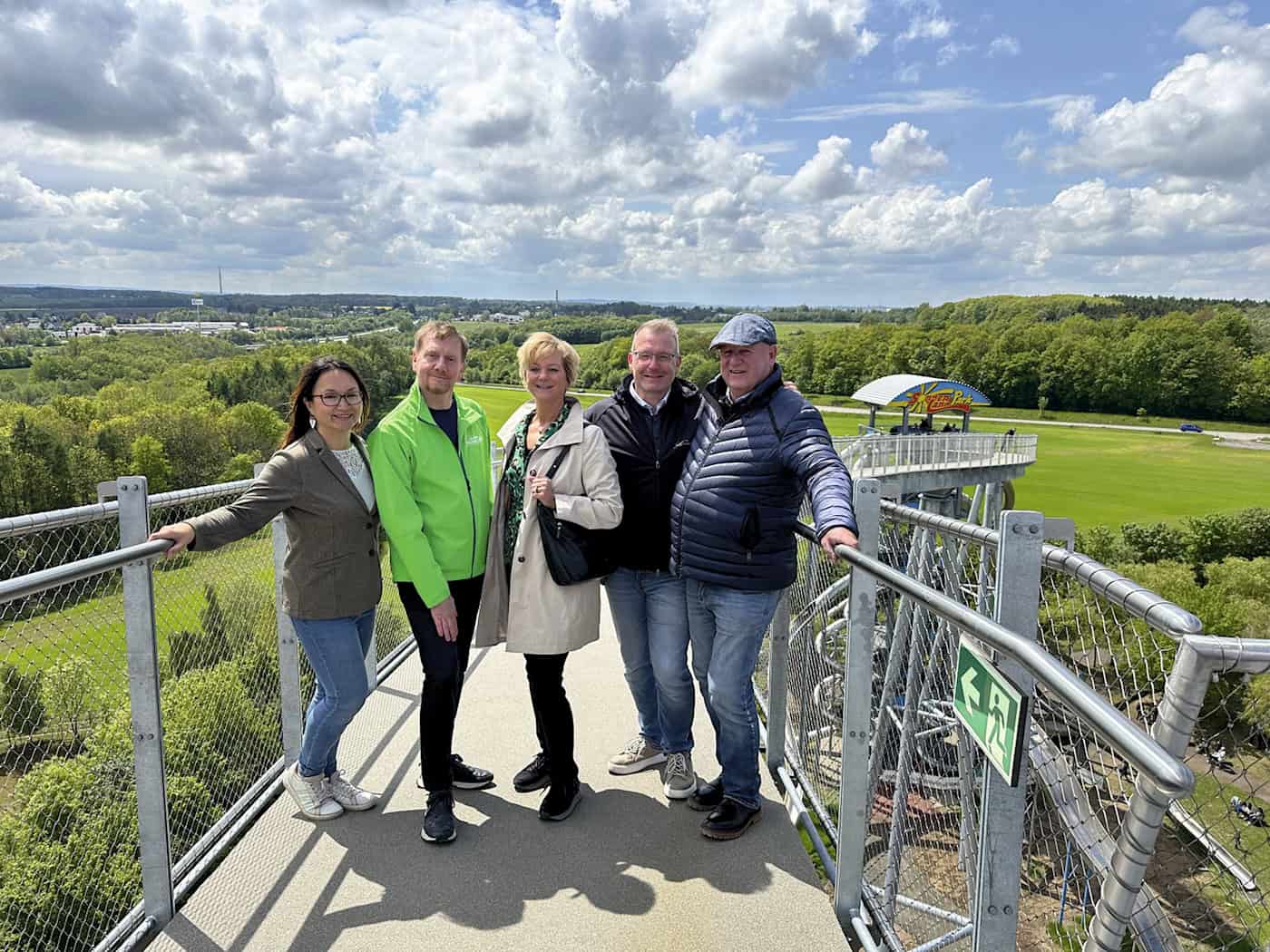 Eröffnung Skywalk Sonnenlandpark Lichtenau 2026. Eine Gruppe von Personen, darunter Michael Kretschmer und weitere offizielle Vertreter, steht in festlicher Atmosphäre im Sonnenlandpark vor einer großen neuen Stahlkonstruktion (Skywalk) und Pyramide; im Hintergrund ist eine Parklandschaft zu sehen.