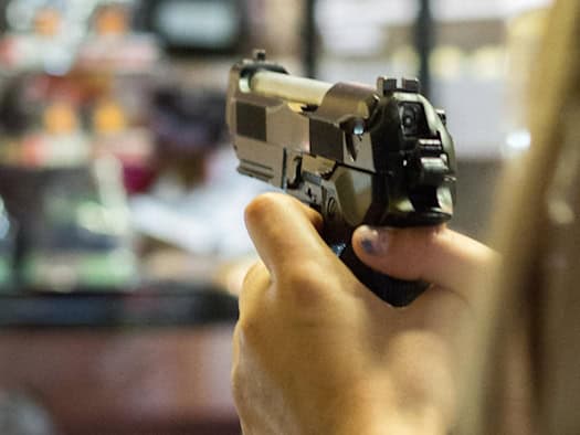 Eine Frau steht auf einer Kirmes an einem Schießstand und zielt mit einer Spielzeugpistole in der Hand auf die Ziele.