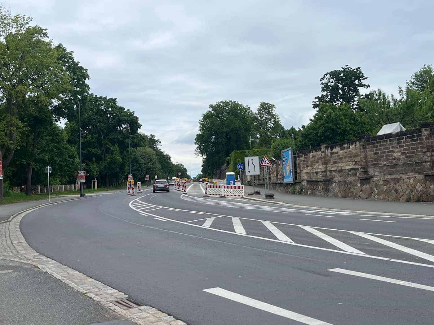 Sanierungsarbeiten auf der Stauffenbergallee in Dresden Die frisch asphaltierte Stauffenbergallee in Dresden mit Baustellenabsperrungen, Verkehrsschildern und einer historischen Steinmauer auf der rechten Seite.