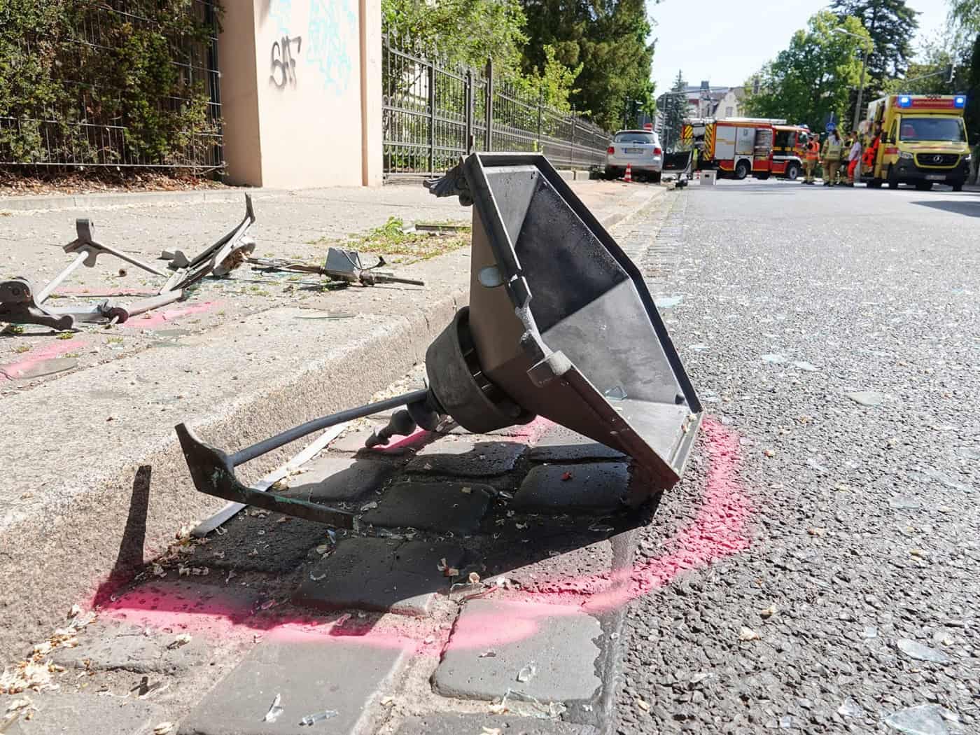 Eine Nahaufnahme der zerstörten historischen Gaslaterne, die nach dem schweren Verkehrsunfall in der Hüblerstraße in Blasewitz auf dem Gehweg liegt. Im Hintergrund sind Feuerwehr und Rettungsdienst im Einsatz.