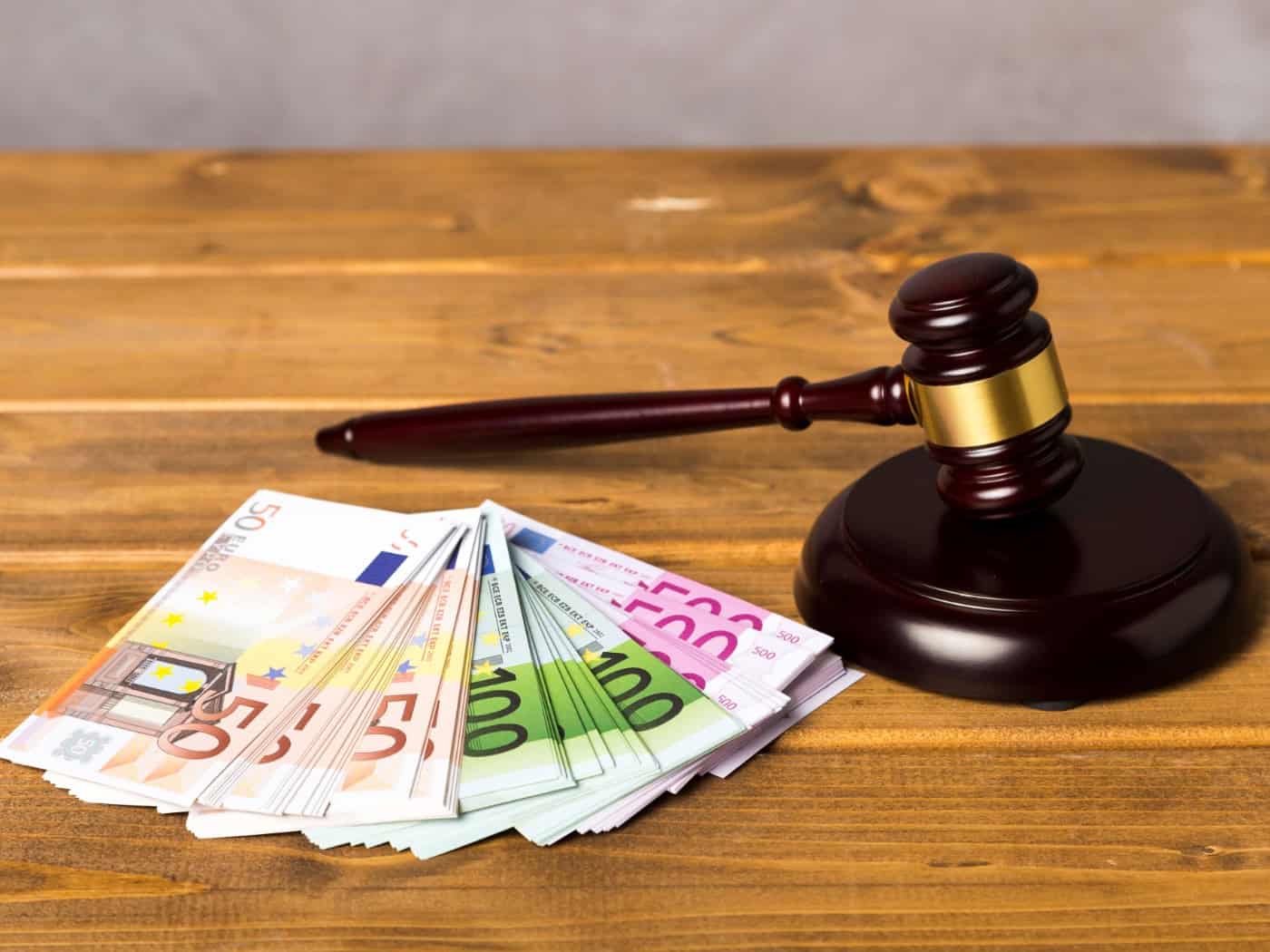 Ein brauner Auktionshammer aus Holz liegt neben mehreren gefächerten Euro-Geldscheinen (50er, 100er und 500er) auf einem hölzernen Tisch.