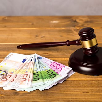 Ein brauner Auktionshammer aus Holz liegt neben mehreren gefächerten Euro-Geldscheinen (50er, 100er und 500er) auf einem hölzernen Tisch.