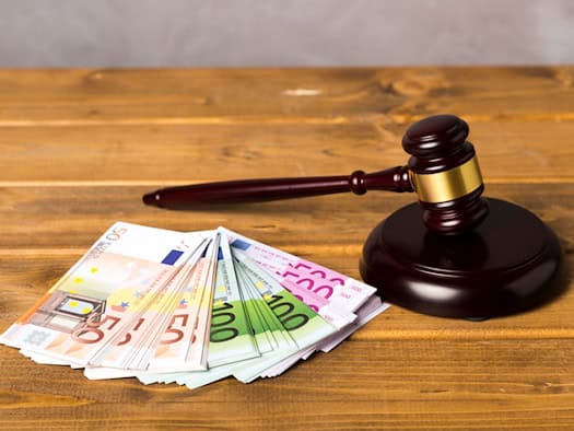 Ein brauner Auktionshammer aus Holz liegt neben mehreren gefächerten Euro-Geldscheinen (50er, 100er und 500er) auf einem hölzernen Tisch.