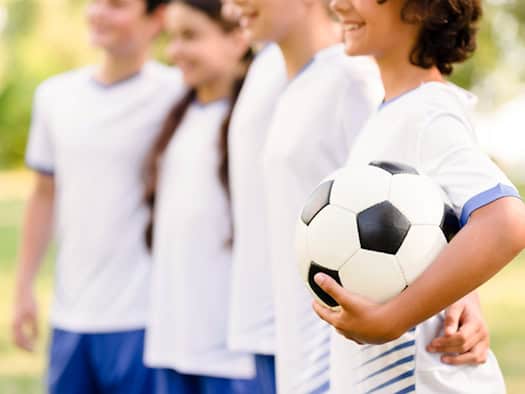 Junger Fußballspieler hält einen Fußball in der Hand – Symbol für Leidenschaft und Teamgeist.