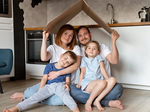 Familie baut gemeinsam ein Haus aus Pappe – Symbol für Sicherheit und Geborgenheit im Zuhause.