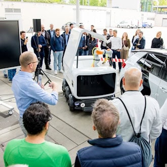Fachpublikum bei der Präsentation eines autonomen Laderoboters im Sportpark Ostra, der ein Elektrofahrzeug mit einem mobilen Akkuwaggon versorgt.