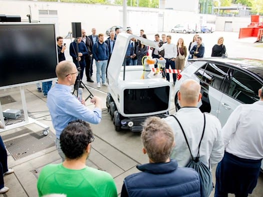 Fachpublikum bei der Präsentation eines autonomen Laderoboters im Sportpark Ostra, der ein Elektrofahrzeug mit einem mobilen Akkuwaggon versorgt.
