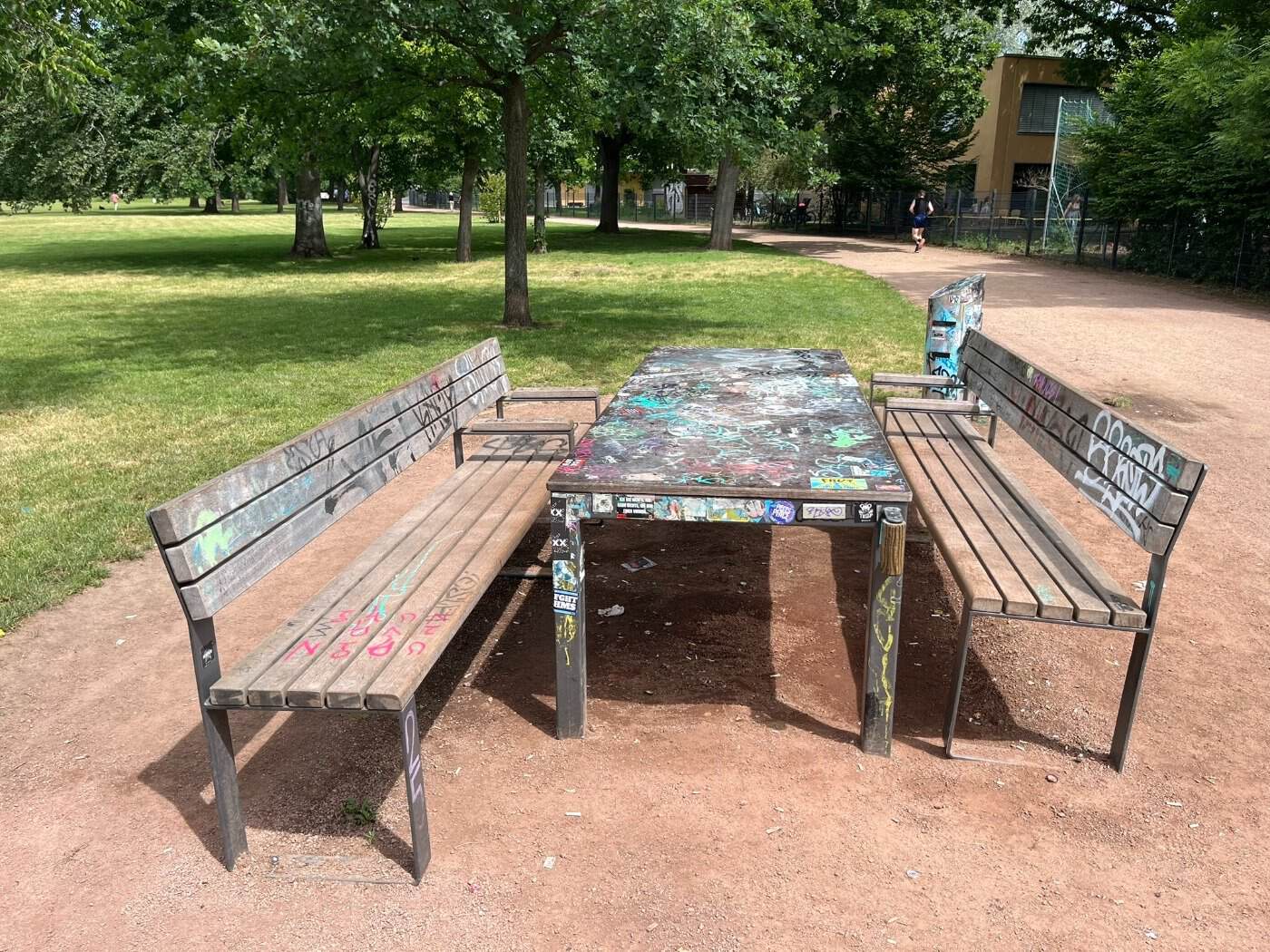 Eine hölzerne, barrierefreie Sitzgruppe mit graffiti-verzierter Tischplatte und zwei Holzbänken auf dem Alaunplatz in Dresden Neustadt.