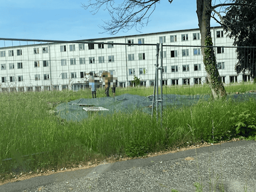 Arbeiter begutachten den mit einer grünen Plane abgedeckten Brandschutt an der Caspar-David-Friedrich-Straße in Dresden; im Hintergrund ist ein großes verlassenes Gebäude mit zerstörten Fenstern zu sehen.