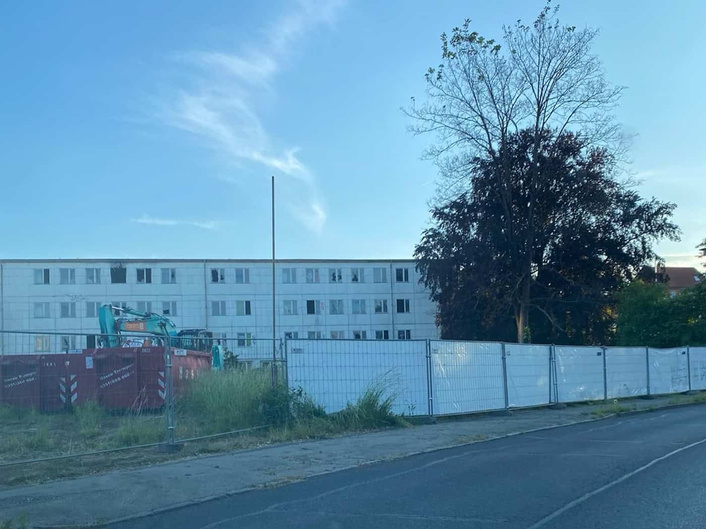 Blick auf die weiß eingezäunte Brandstelle an der Caspar-David-Friedrich-Straße in Dresden-Strehlen mit einem Schuttcontainer und einem Bagger vor einem Wohngebäude.