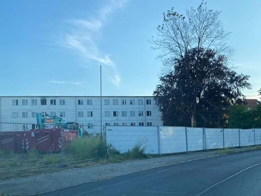 Blick auf die weiß eingezäunte Brandstelle an der Caspar-David-Friedrich-Straße in Dresden-Strehlen mit einem Schuttcontainer und einem Bagger vor einem Wohngebäude.