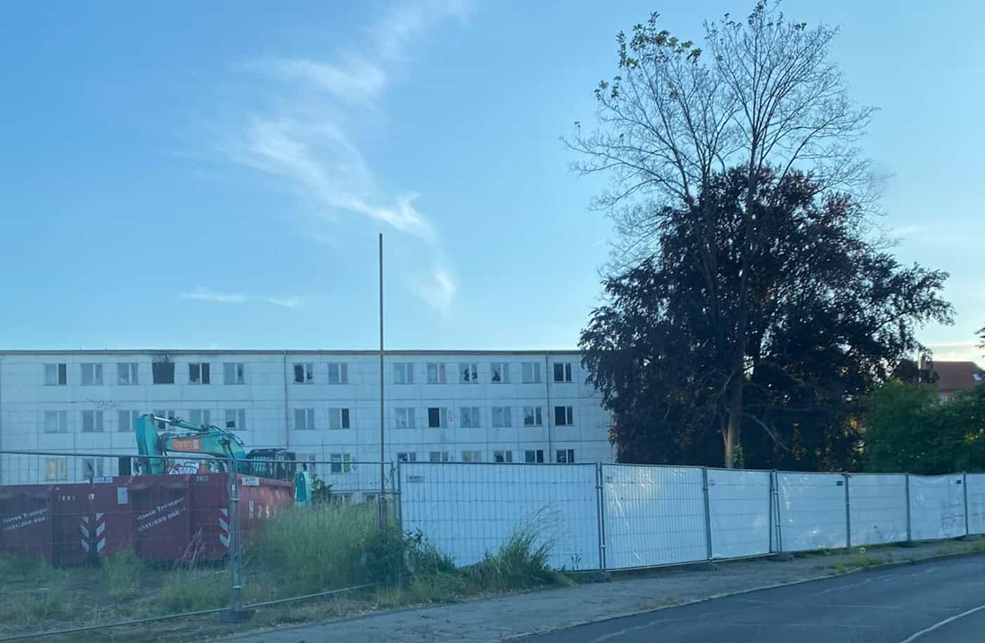 Schutträumung und Asbestentsorgung in Dresden-Strehlen Blick auf die weiß eingezäunte Brandstelle an der Caspar-David-Friedrich-Straße in Dresden-Strehlen mit einem Schuttcontainer und einem Bagger vor einem Wohngebäude.