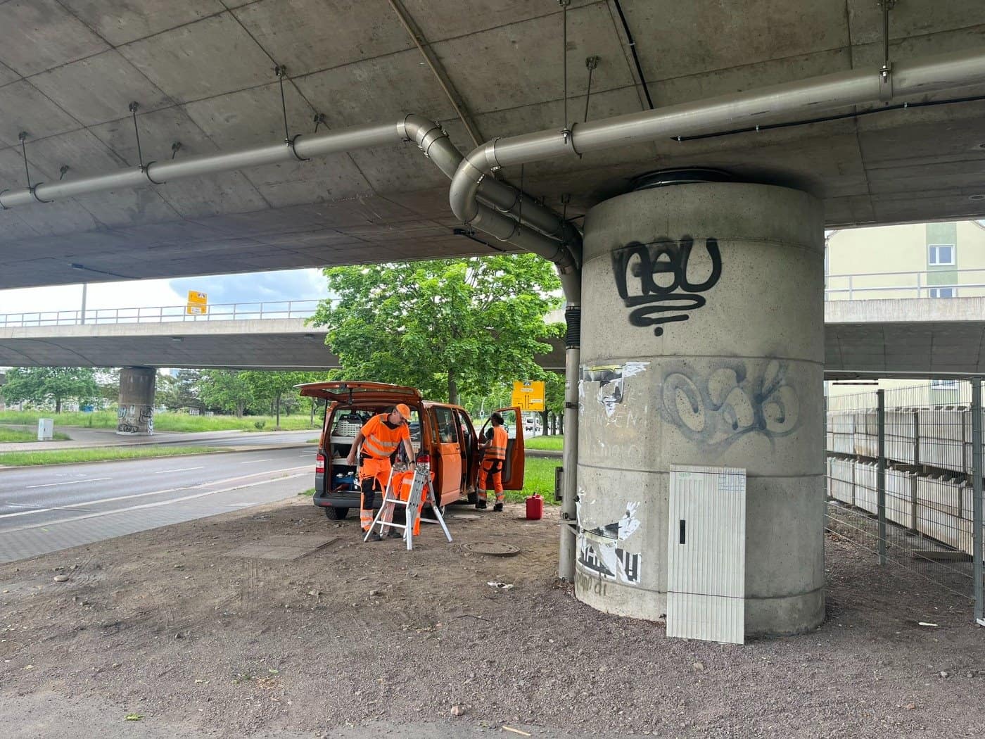 Bauarbeiter in orangefarbener Warnkleidung entladen Werkzeug aus einem Kleintransporter im Bereich eines Betonpfeilers unterhalb der Brücke Budapester Straße in Dresden.