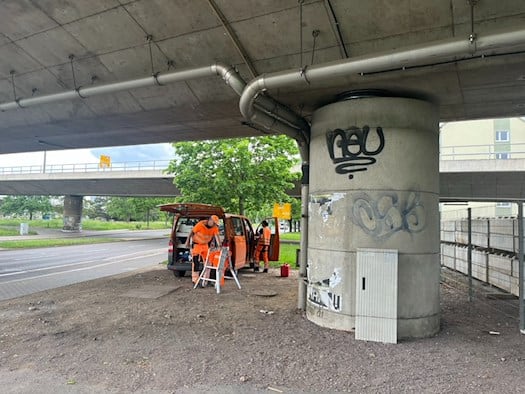 Bauarbeiter in orangefarbener Warnkleidung entladen Werkzeug aus einem Kleintransporter im Bereich eines Betonpfeilers unterhalb der Brücke Budapester Straße in Dresden.