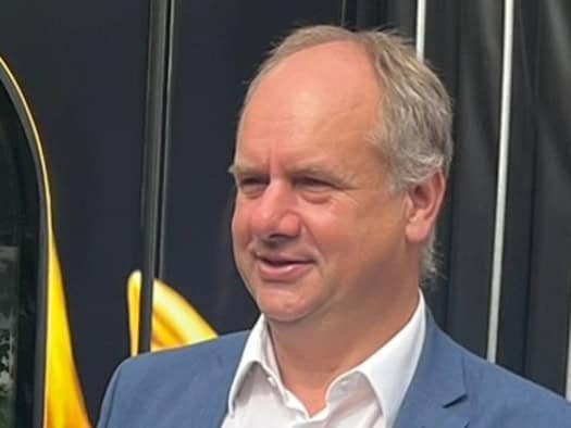 Porträtaufnahme von Dresdens Oberbürgermeister Dirk Hilbert im Dreiviertelprofil vor einem dunklen Hintergrund mit gelben Akzenten.  Er trägt ein blaues Sakko über einem offenen, weißen Hemd ohne Krawatte und blickt mit einem leichten Lächeln nach links.