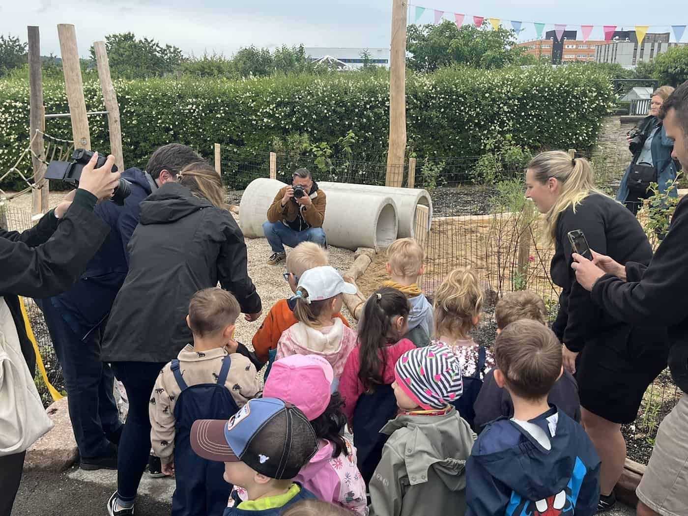 Eine Menschenmenge aus Kindern und Erwachsenen steht auf dem Spielplatz Frauensteiner Platz. Ein Fotograf in brauner Jacke hockt hinter zwei Betonröhren und fotografiert die Kinder.