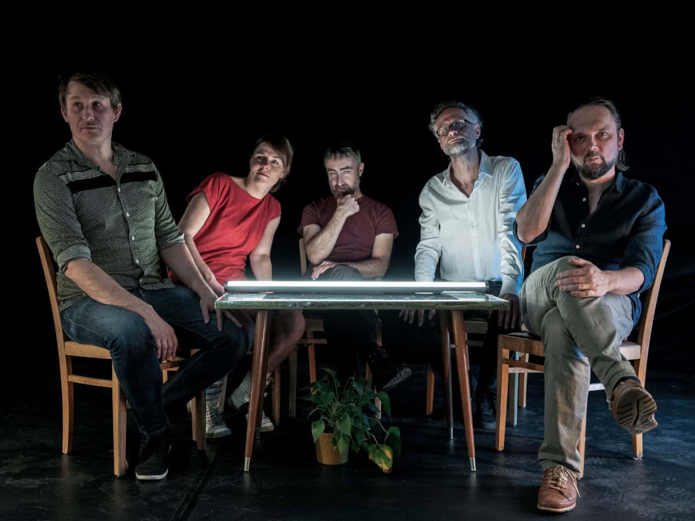 Die fünf Bandmitglieder von Fiffy & The Kids sitzen im schummrigen Licht um einen von unten beleuchteten Tisch vor schwarzem Hintergrund.