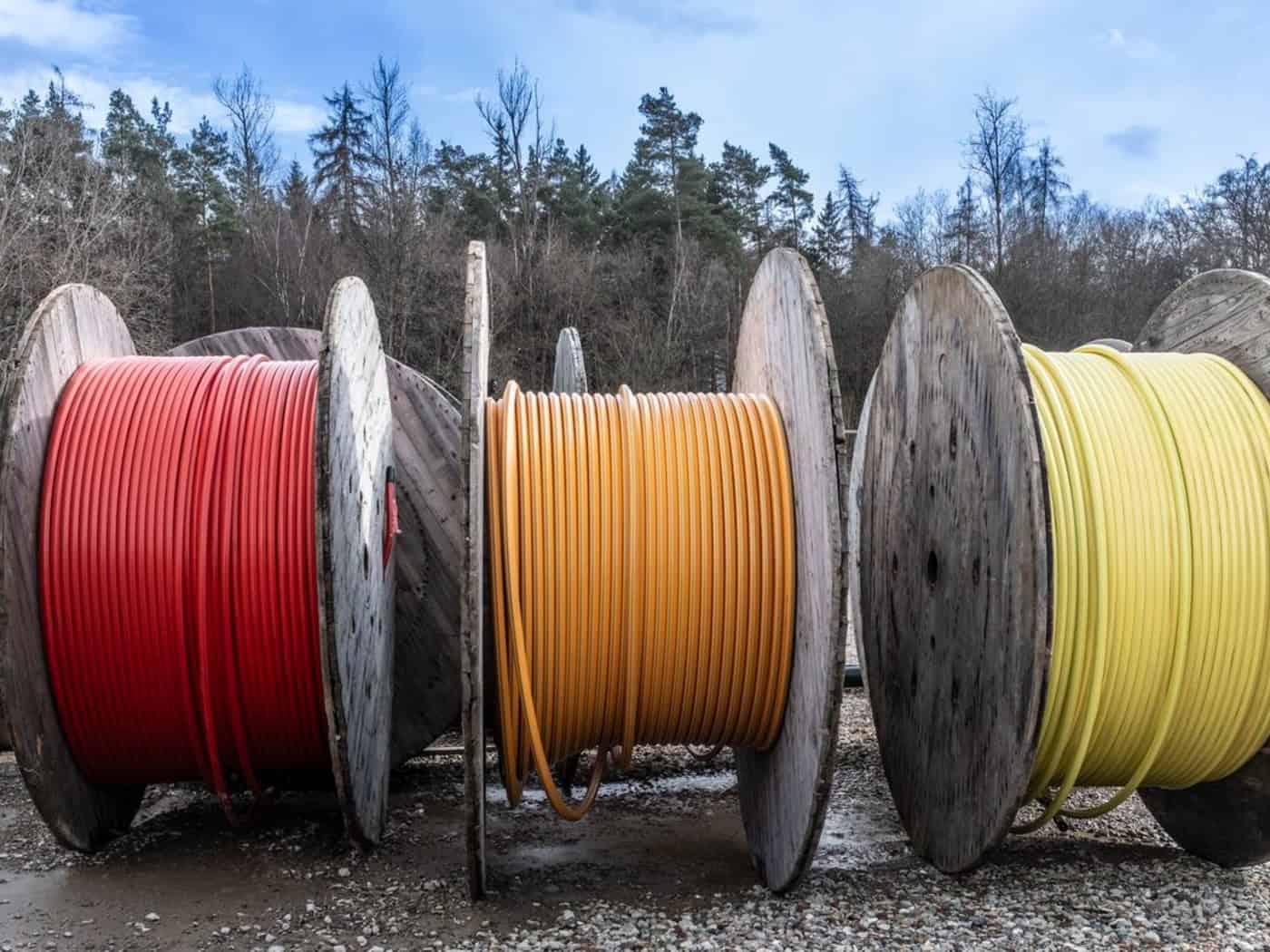 3 große Rollen mit aufgewickeltem Glasfaserkabel auf einer Baustelle