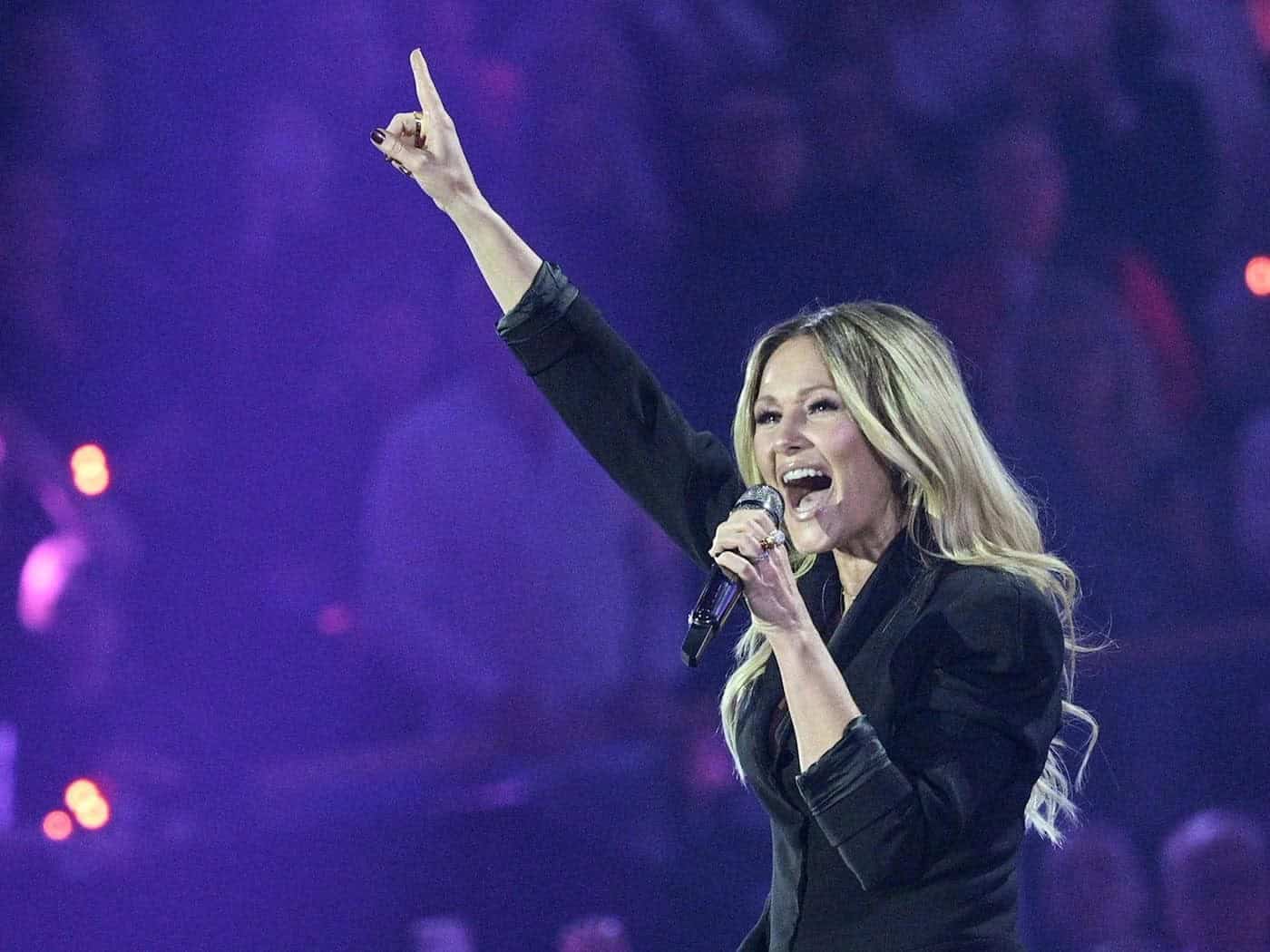 Die Sängerin Helene Fischer singt im schwarzen Blazer mit dynamisch erhobenem Zeigefinger auf einer violett ausgeleuchteten Konzertbühne.