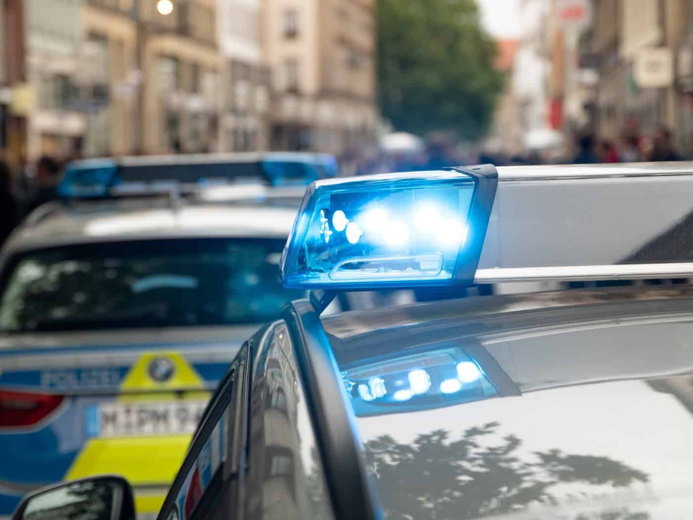 Nahaufnahme eines leuchtenden blauen Signallichts auf dem Dach eines Polizeifahrzeugs im städtischen Raum (Symbolbild).