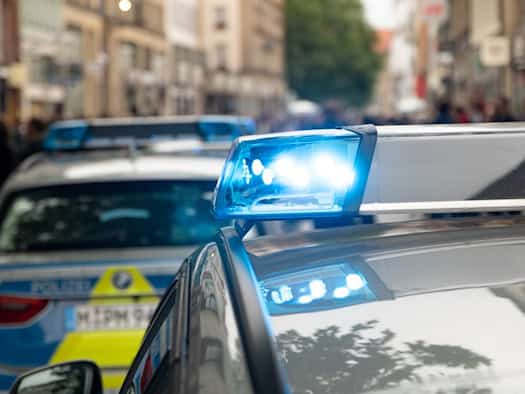 Nahaufnahme eines leuchtenden blauen Signallichts auf dem Dach eines Polizeifahrzeugs im städtischen Raum (Symbolbild).