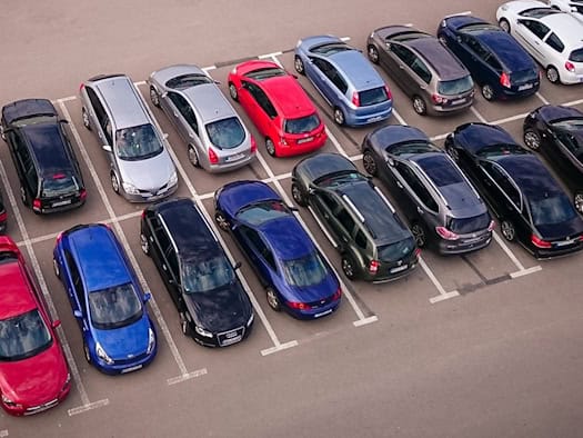 Zahlreiche farbige Autos parken ordentlich nebeneinander in markierten Buchten auf einem asphaltierten Parkplatz.