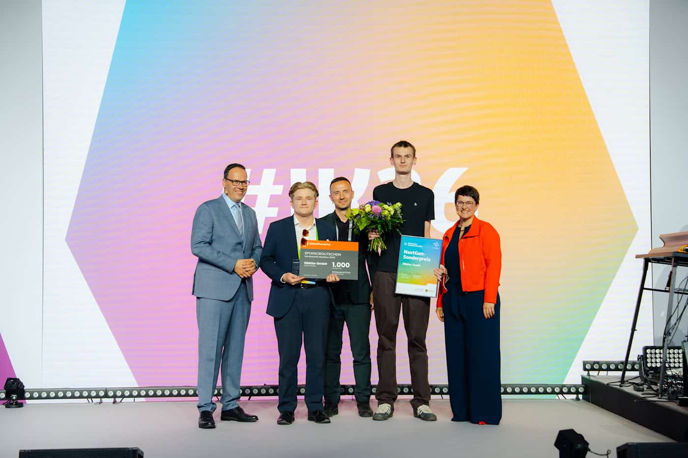 Elbklar GmbH gewinnt den NextGen-Sonderpreis 2026 Drei junge Männer stehen auf einer Bühne und halten einen Sponsorengutschein über 1.000 Euro sowie eine NextGen-Sonderpreis-Urkunde für die Elbklar GmbH in die Kamera. Flankiert werden sie von zwei Offiziellen.