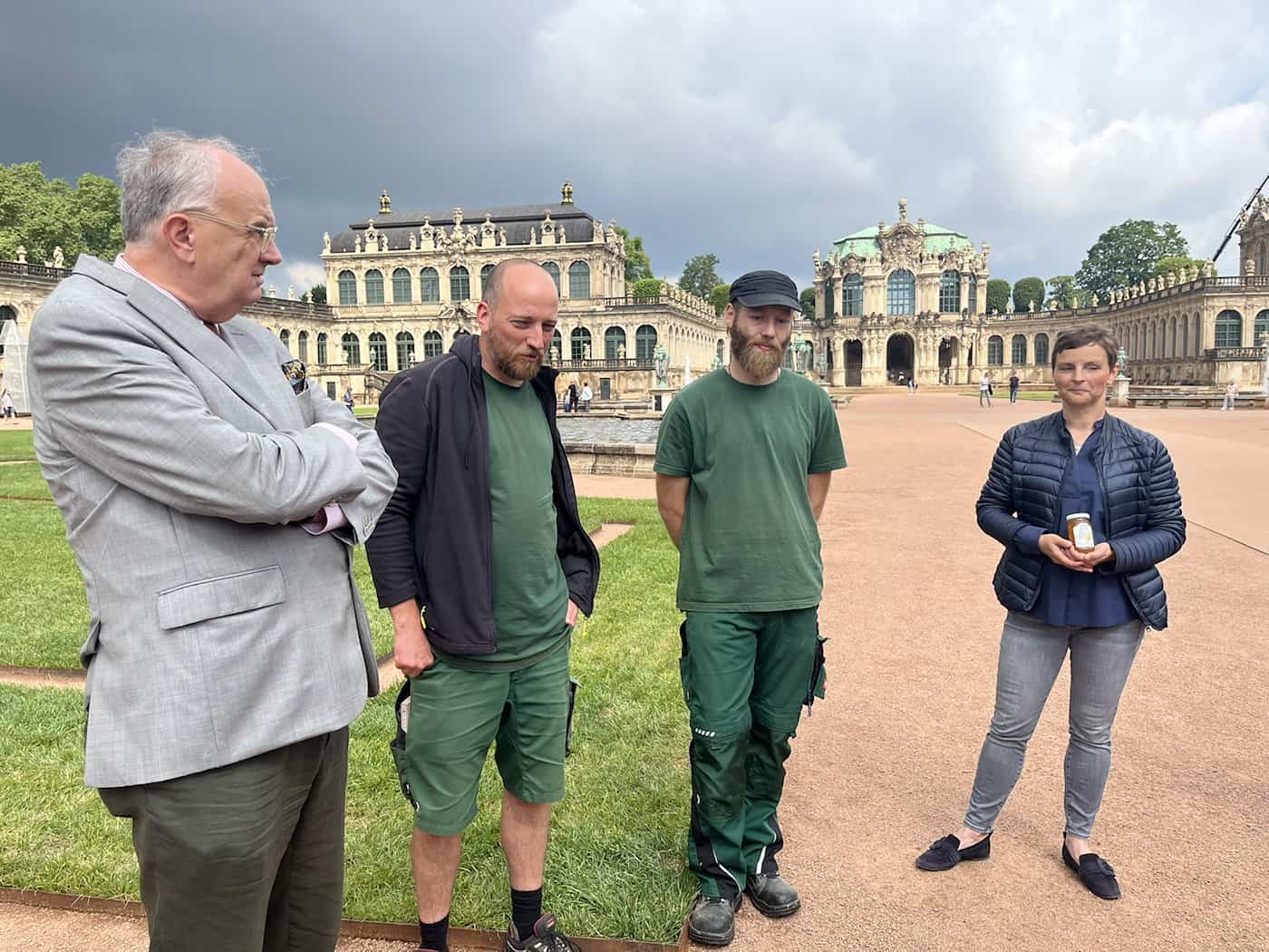 Schlossleiterin Yvonne Aulhorn präsentiert ein Glas Marmelade, umgeben von Gärtnern und einem weiteren Beteiligten im Zwingerhof.