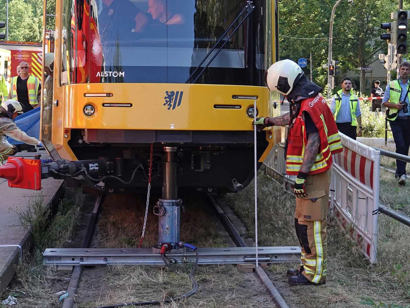 Einsatzkräfte der Feuerwehr Dresden heben eine gelbe Straßenbahn mit hydraulischem Gerät an der Haltestelle Reichenbachstraße an.