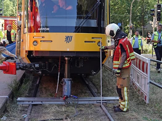 Einsatzkräfte der Feuerwehr Dresden heben eine gelbe Straßenbahn mit hydraulischem Gerät an der Haltestelle Reichenbachstraße an.