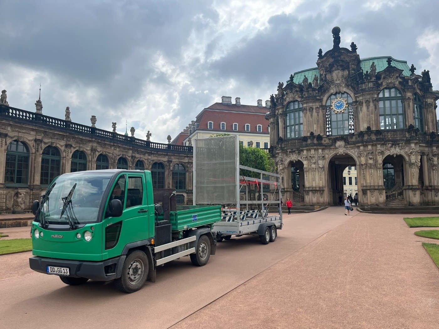 Ein grüner Multicar zieht einen Spezialanhänger mit einer großen Pomeranze durch den Dresdner Zwingerhof.